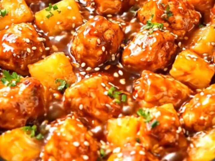 A black slow cooker filled with glistening, tender chicken pieces and pineapple chunks coated in a sticky glaze