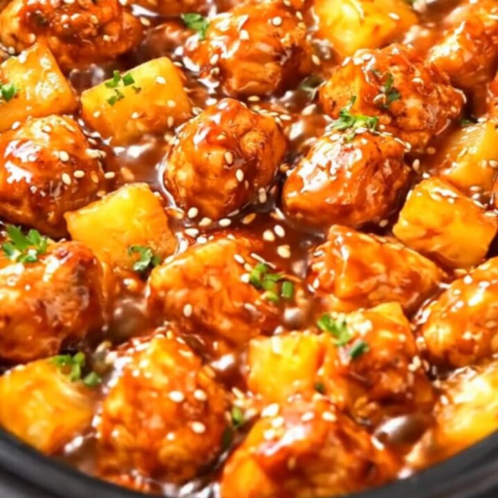 A black slow cooker filled with glistening, tender chicken pieces and pineapple chunks coated in a sticky glaze