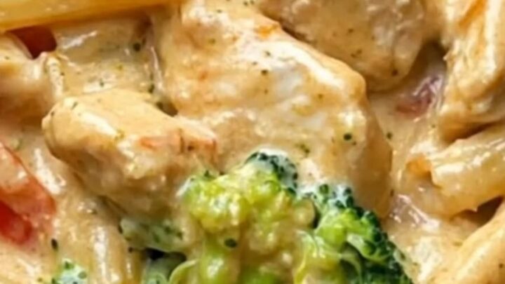 A steaming plate of creamy chicken penne pasta with bright green broccoli and red peppers in a glossy sauce.