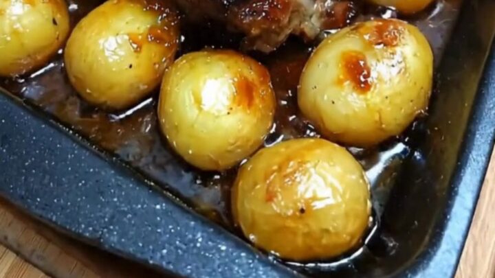 A succulent honey glazed roast pork topped with fresh rosemary in a roasting pan beside caramelized baby onions