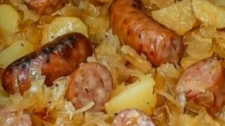 A rustic cast-iron skillet filled with caramelized kielbasa coins, golden-brown cubed potatoes, and steaming sauerkraut.