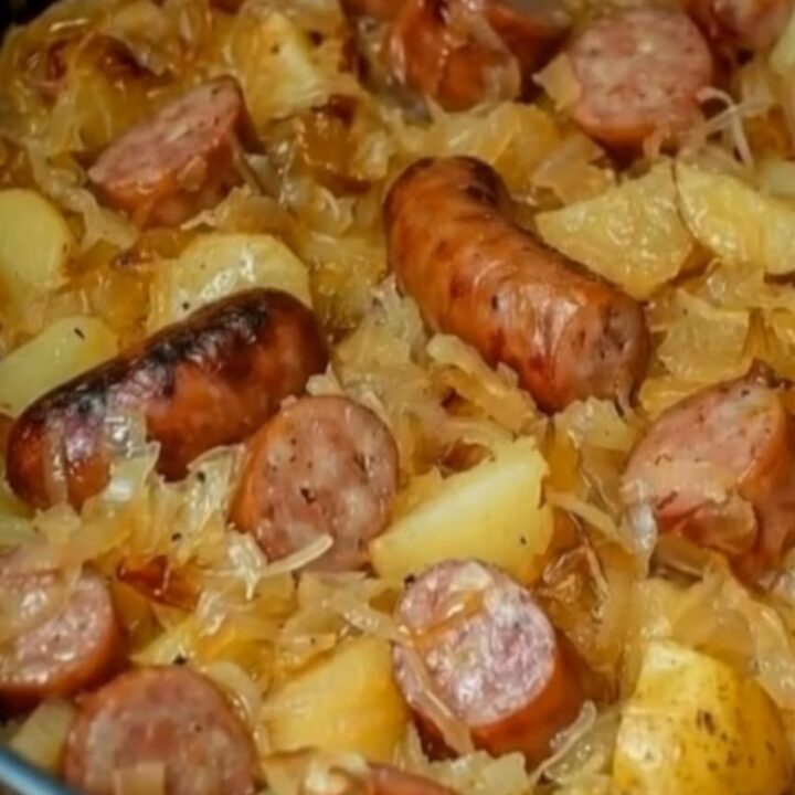 A rustic cast-iron skillet filled with caramelized kielbasa coins, golden-brown cubed potatoes, and steaming sauerkraut.
