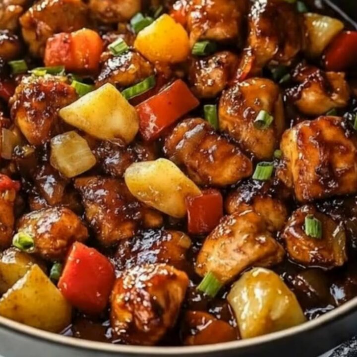 A hot skillet filled with sticky glazed chicken, juicy pineapple chunks, vibrant bell peppers, and chopped green onions.