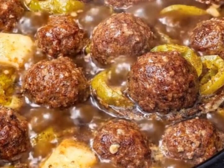 A close-up of a glistening Mississippi meatball dripping with rich au jus gravy and melted butter on a spoon.