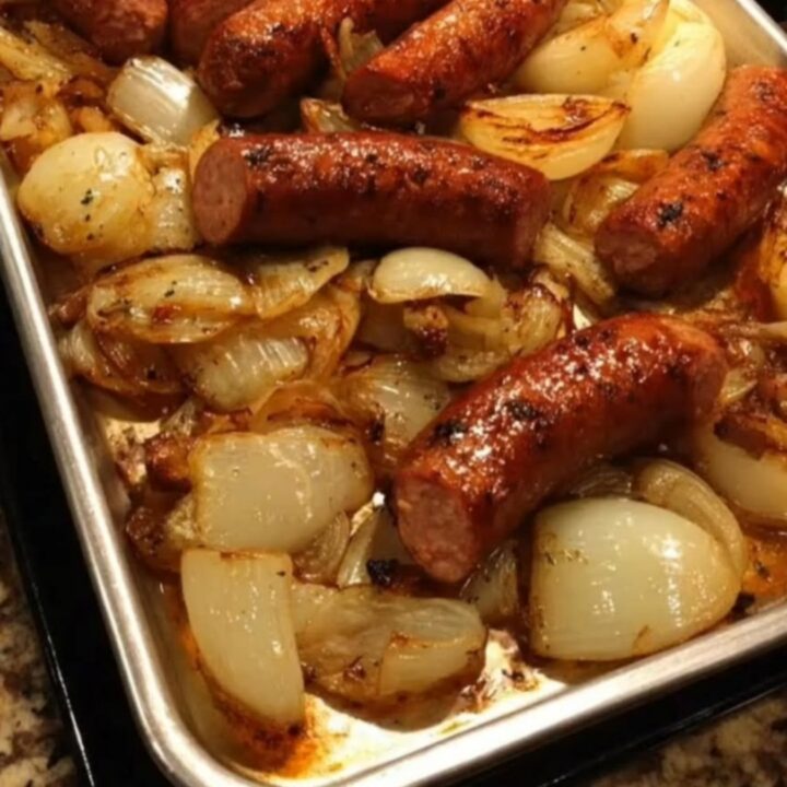 Slices of juicy roasted sausage mixed with sweet, golden-brown caramelized onions in a metal baking tray.