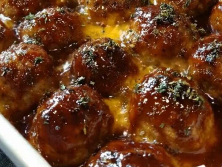 A white ceramic baking dish filled with glazed BBQ meatballs covered in melted, bubbling mozzarella cheese and parsley.