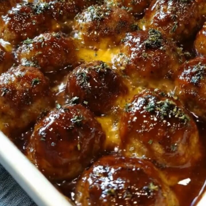 A white ceramic baking dish filled with glazed BBQ meatballs covered in melted, bubbling mozzarella cheese and parsley.