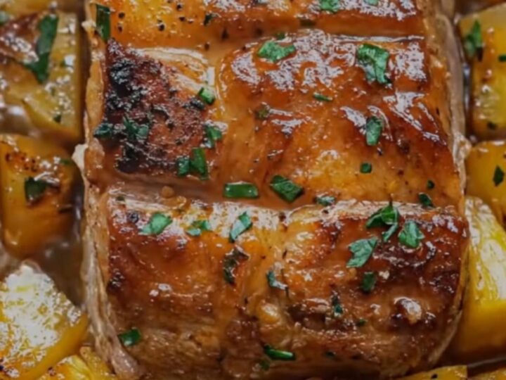 A glistening, sliced slow cooker pineapple pork loin served on a platter, surrounded by golden roasted pineapple chunks.