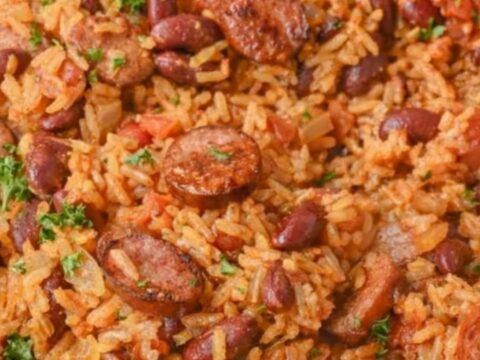 A steaming skillet of Cajun red beans and rice topped with glazed, sliced smoked sausage and fresh parsley.