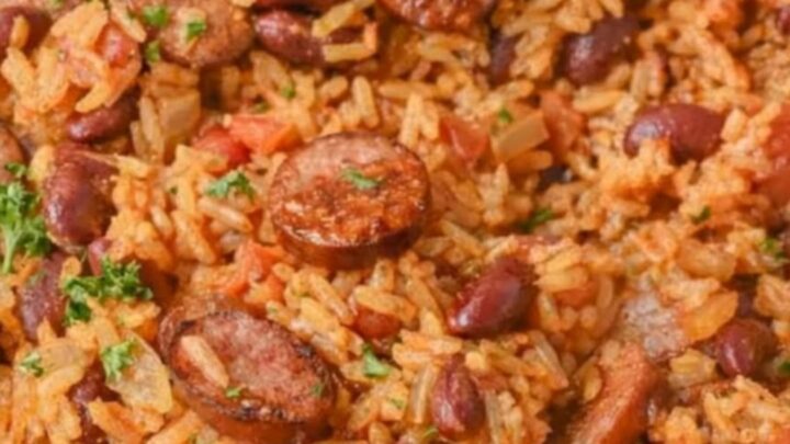 A steaming skillet of Cajun red beans and rice topped with glazed, sliced smoked sausage and fresh parsley.