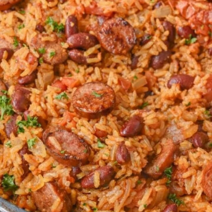 A steaming skillet of Cajun red beans and rice topped with glazed, sliced smoked sausage and fresh parsley.