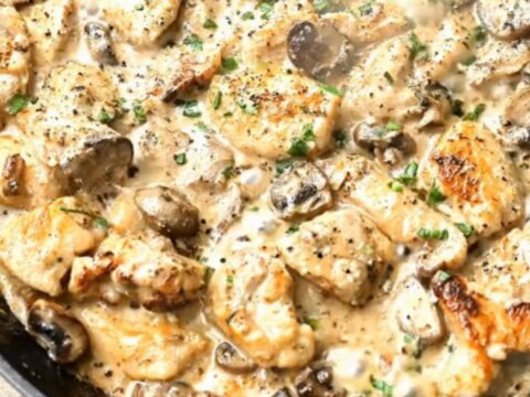 A black cast-iron skillet filled with golden-brown chicken pieces and tender mushrooms in a rich cream sauce