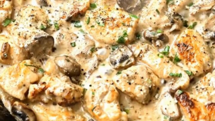 A black cast-iron skillet filled with golden-brown chicken pieces and tender mushrooms in a rich cream sauce
