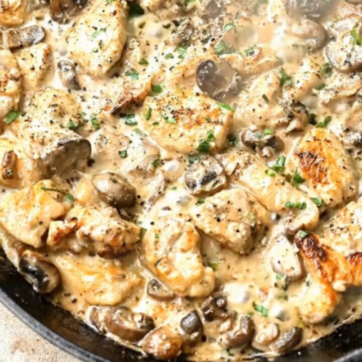 A black cast-iron skillet filled with golden-brown chicken pieces and tender mushrooms in a rich cream sauce