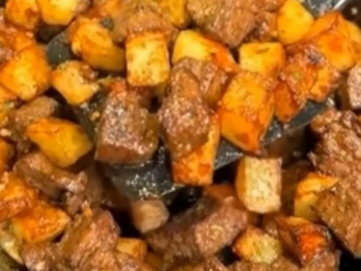 A seasoned cast-iron skillet filled with juicy, browned steak bites and crispy golden diced potatoes glistening with melted