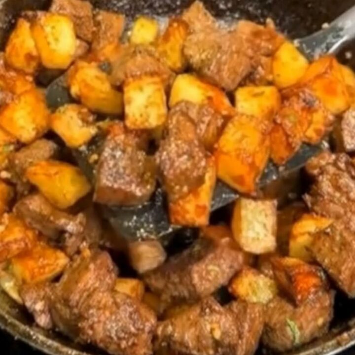 A seasoned cast-iron skillet filled with juicy, browned steak bites and crispy golden diced potatoes glistening with melted