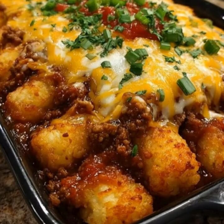 A steaming black rectangular baking dish filled with Sloppy Joe tater tot casserole
