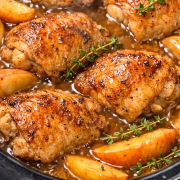 Slow-cooked browned chicken thighs with sliced apples and thyme sprigs simmering in a slow cooker