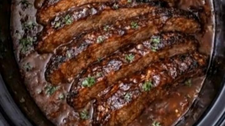 A slow cooker filled with glistening, sliced beef brisket coated in rich barbecue sauce and garnished with fresh herbs