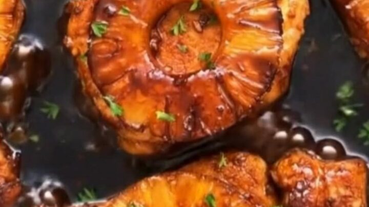 Juicy seared pork chops topped with grilled pineapple slices and a glossy, bubbling teriyaki glaze in a skillet.