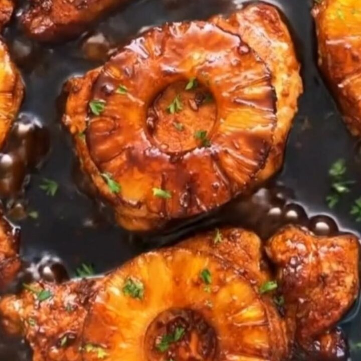 Juicy seared pork chops topped with grilled pineapple slices and a glossy, bubbling teriyaki glaze in a skillet.