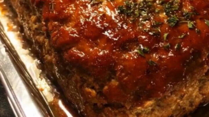 A thick, juicy slice of meatloaf being cut with a sharp knife, showing a glistening caramelized glaze on top.