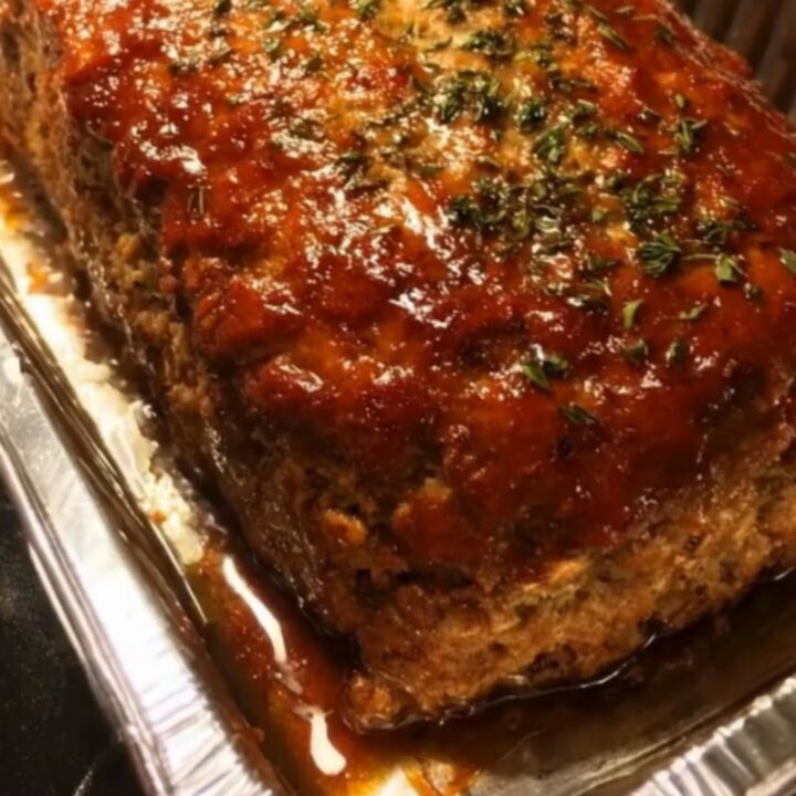 A thick, juicy slice of meatloaf being cut with a sharp knife, showing a glistening caramelized glaze on top.