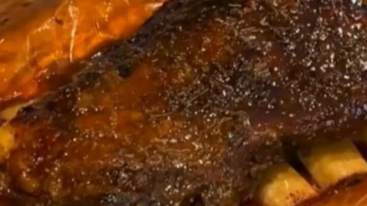 A rack of glossy, sticky smoked beef ribs resting on rustic butcher paper under warm light.
