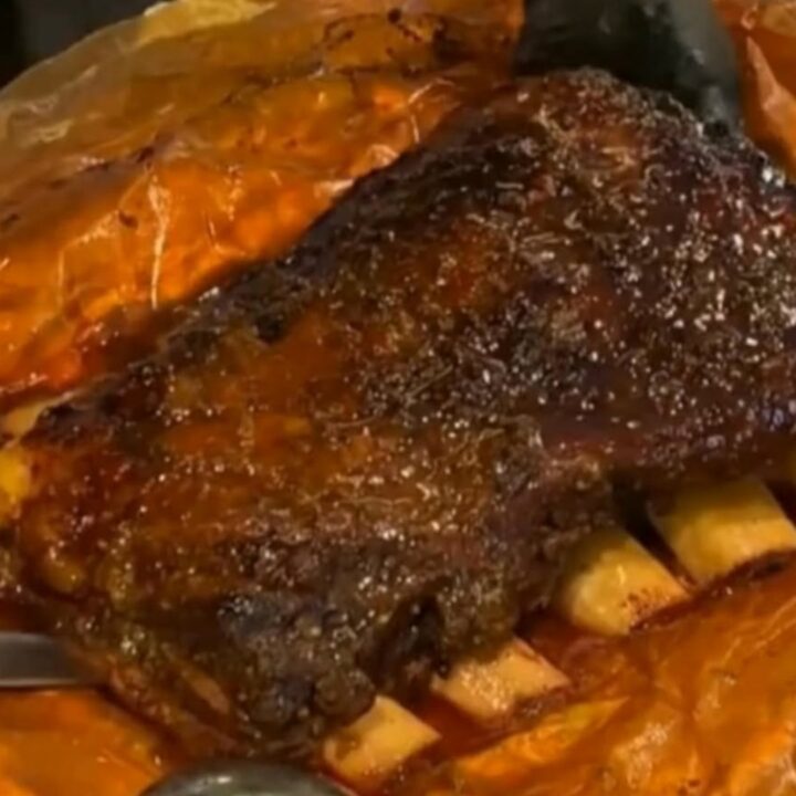 A rack of glossy, sticky smoked beef ribs resting on rustic butcher paper under warm light.