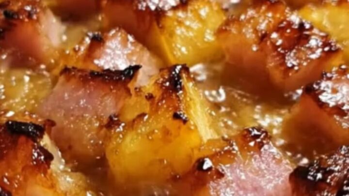 A white baking dish filled with caramelized brown sugar ham cubes and bubbling golden pineapple chunks.