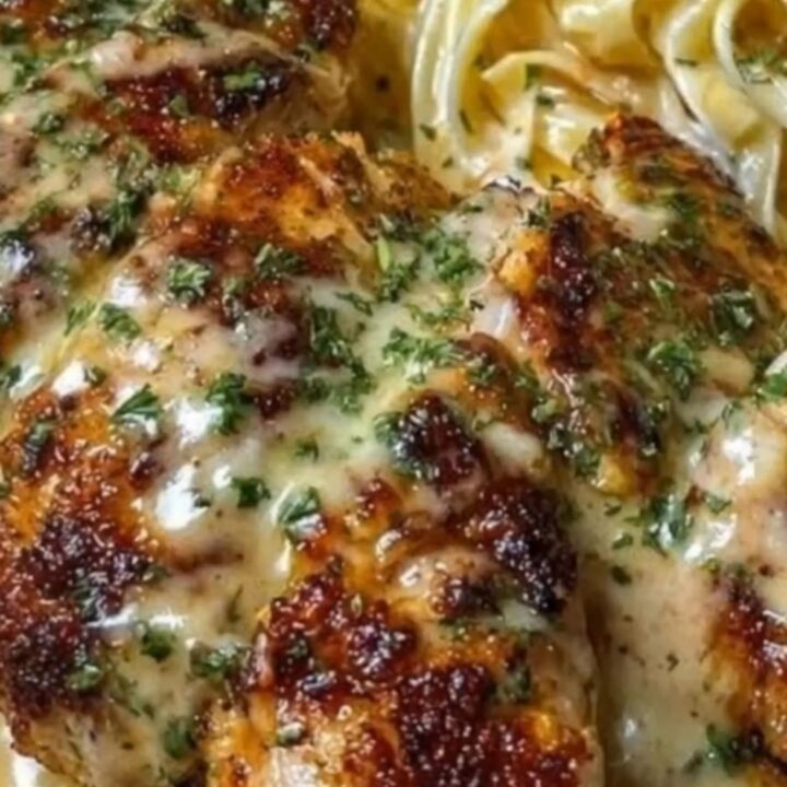 A plate of creamy fettuccine swirled next to sliced golden-brown garlic chicken with steam rising.