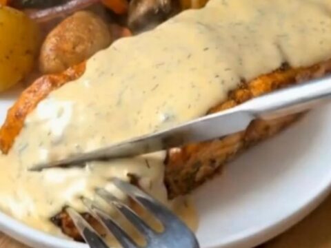 Tender herb-crusted salmon fillet drizzled with creamy dill sauce next to roasted potatoes and broccoli on a plate