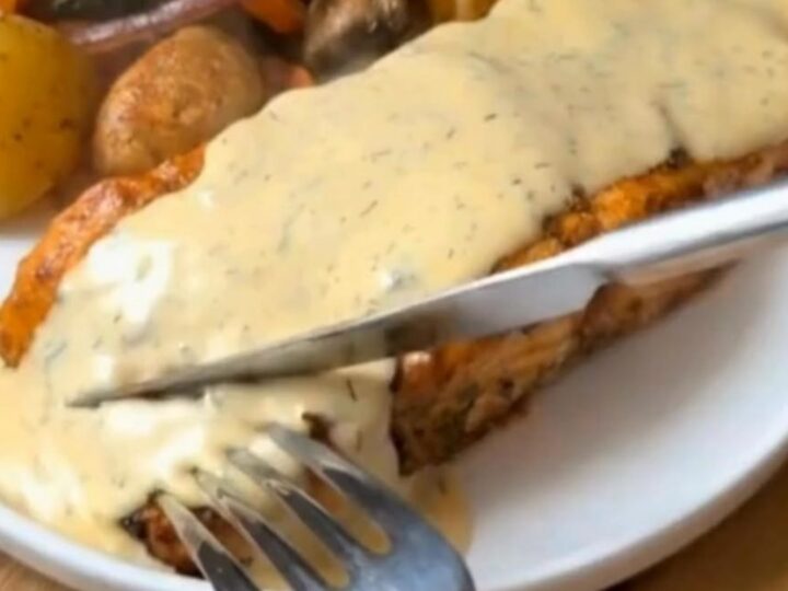 Tender herb-crusted salmon fillet drizzled with creamy dill sauce next to roasted potatoes and broccoli on a plate