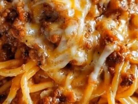 A close-up of glistening garlic butter spaghetti layered with seasoned ground beef and melted cheddar parmesan cheese.