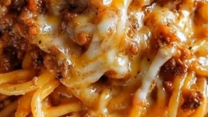 A close-up of glistening garlic butter spaghetti layered with seasoned ground beef and melted cheddar parmesan cheese.