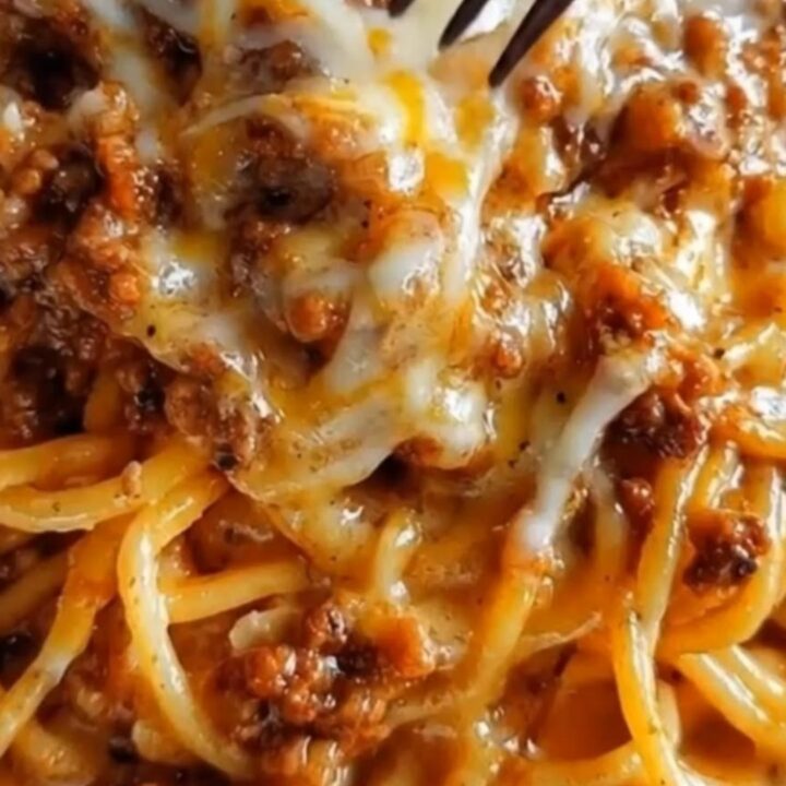 A close-up of glistening garlic butter spaghetti layered with seasoned ground beef and melted cheddar parmesan cheese.