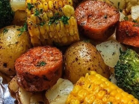A freshly unwrapped foil packet revealing seared sausage slices, tender baby potatoes, corn, and broccoli.