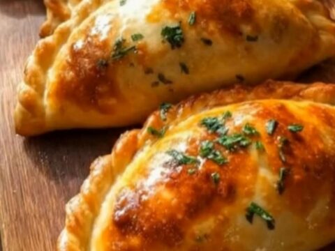 A close-up of golden-brown Argentine beef empanadas garnished with fresh parsley on a wooden board.