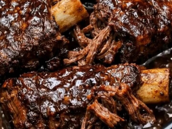 Glistening stout braised beef short ribs coated in a rich dark gravy inside a black slow cooker pot