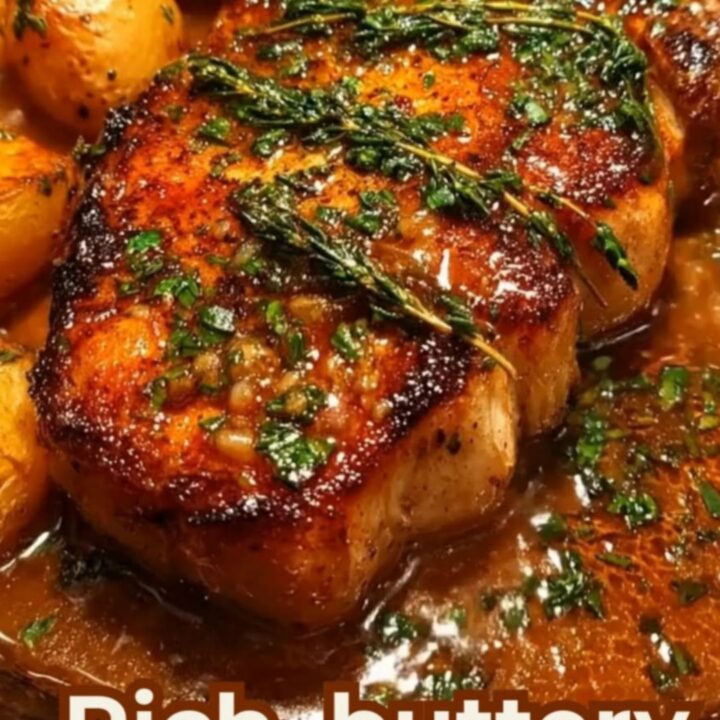 A seasoned cast-iron skillet containing seared pork chops and golden baby potatoes glistening with herb butter.