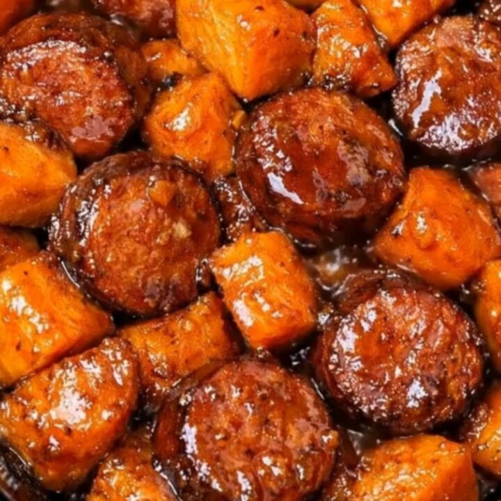 A slow cooker filled with glistening, caramelized smoked sausage rounds and tender, glazed sweet potato cubes.