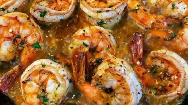 Sizzling garlic butter shrimp garnished with fresh chopped parsley served hot in a rustic black cast iron skillet.