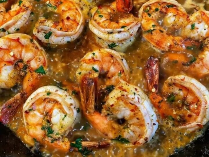 Sizzling garlic butter shrimp garnished with fresh chopped parsley served hot in a rustic black cast iron skillet.