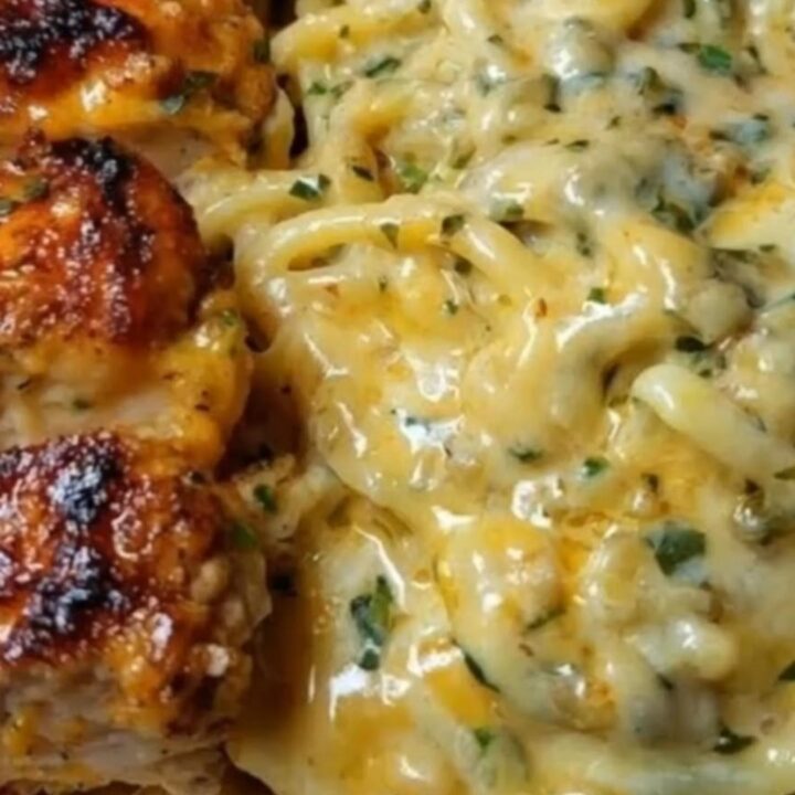A close-up shot of creamy three-cheese spaghetti topped with perfectly sliced seared Cajun chicken breasts and fresh parsley.