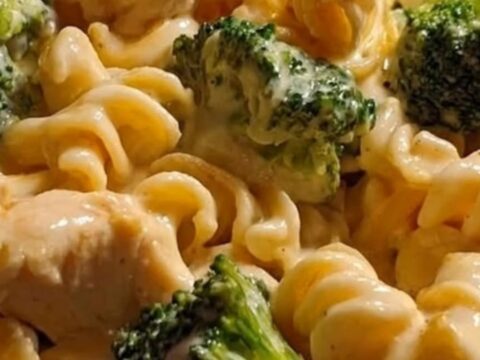 A grey bowl filled with steaming, cheese-coated rotini pasta, golden chicken chunks, and bright green broccoli florets.