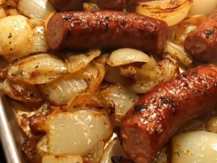 A silver sheet pan filled with charred smoked sausage links and sweet caramelized onion quarters.