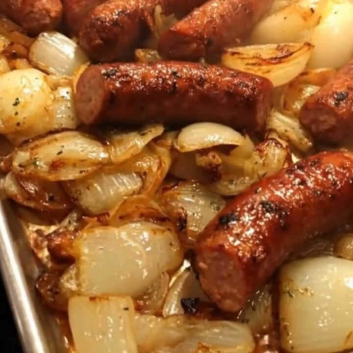 A silver sheet pan filled with charred smoked sausage links and sweet caramelized onion quarters.