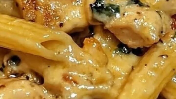 A steaming bowl of creamy penne tossed with golden-brown diced chicken and wilted green baby spinach.
