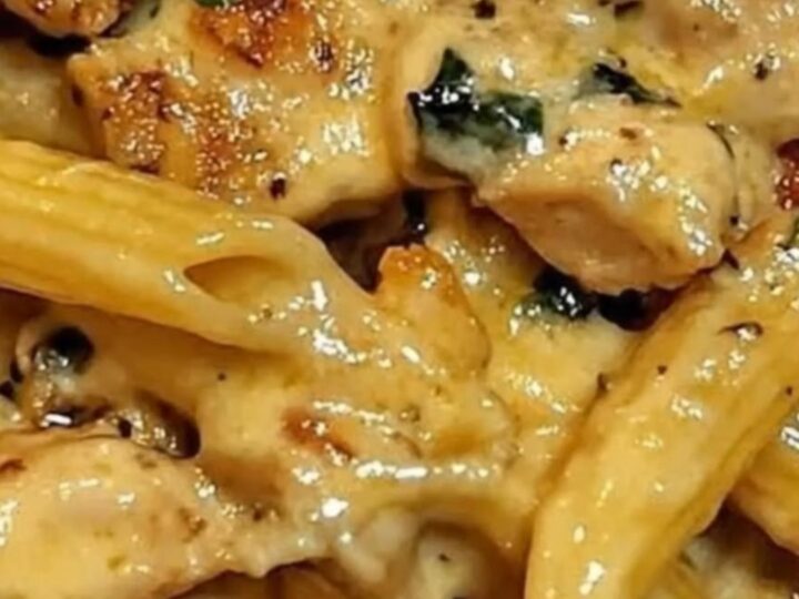 A steaming bowl of creamy penne tossed with golden-brown diced chicken and wilted green baby spinach.