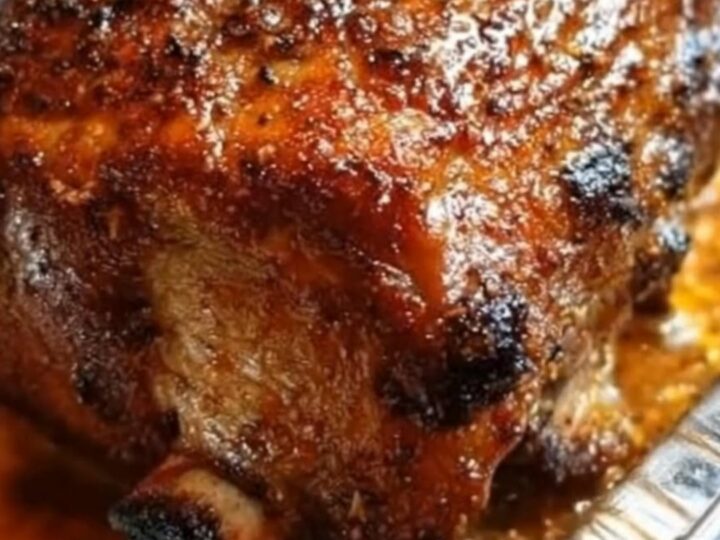 A glistening, herb-crusted glazed turkey roast resting in a foil pan surrounded by savory drippings.